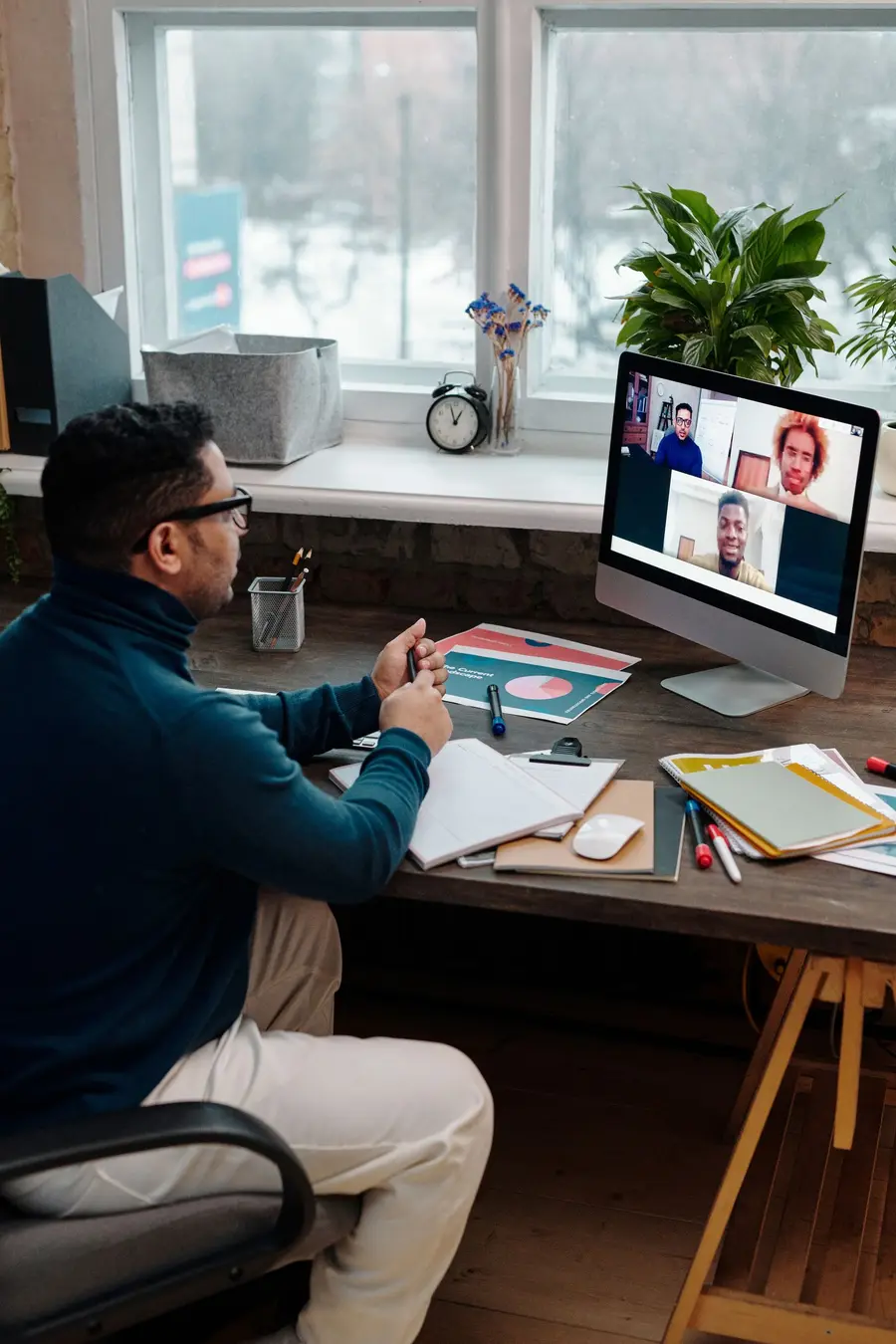 A business owner on a video call at his desk, with notes and charts in front of him