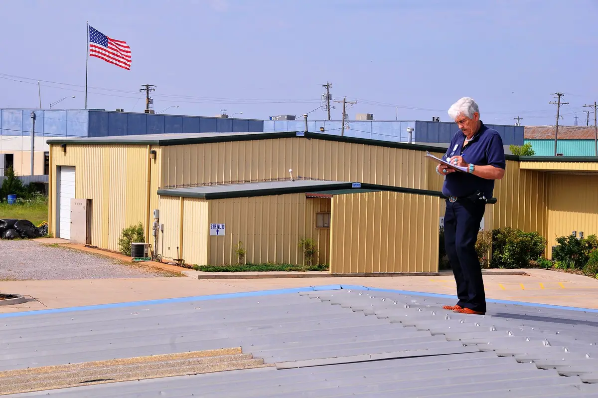 Inspector writing notes while standing on a storm-damaged metal roof