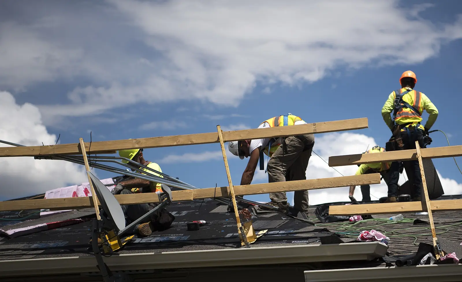 Roofing crew in safety harnesses replacing asphalt shingles on a house roof